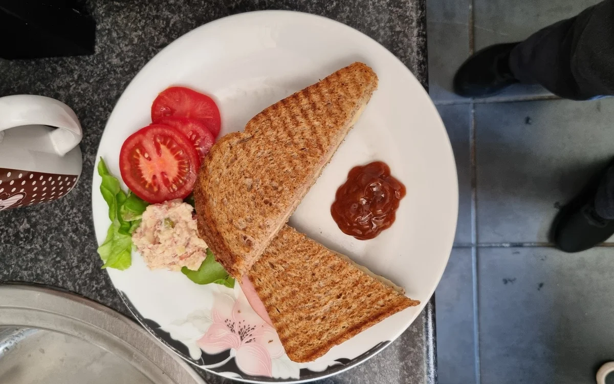 Bord met twee toastjes, tomatenplakken, ham, salade en sauzen.