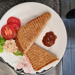 Bord met twee toastjes, tomatenplakken, ham, salade en sauzen.