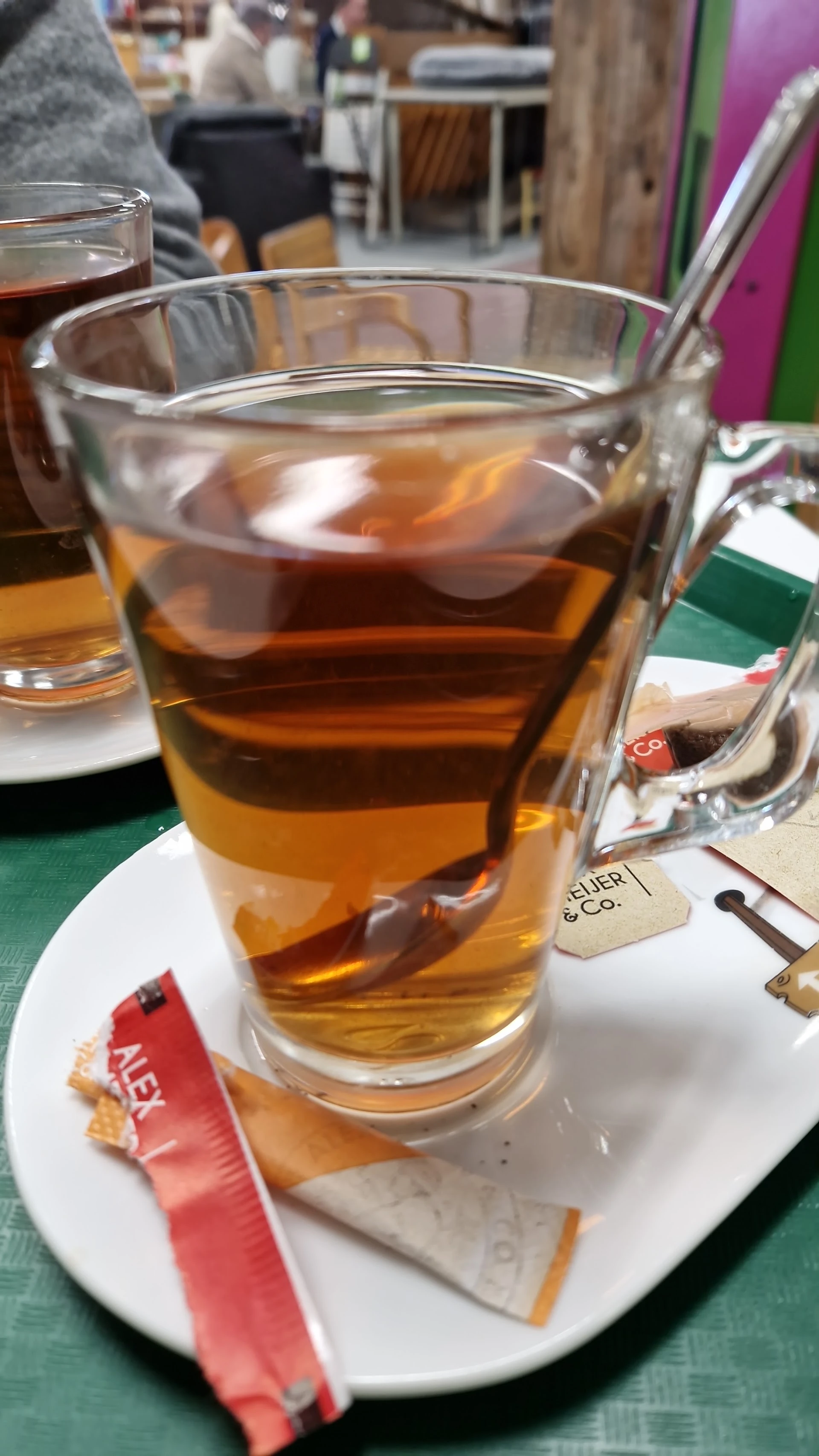 Glas met thee en theebuiltje op een witte onderzetters met winkellogo