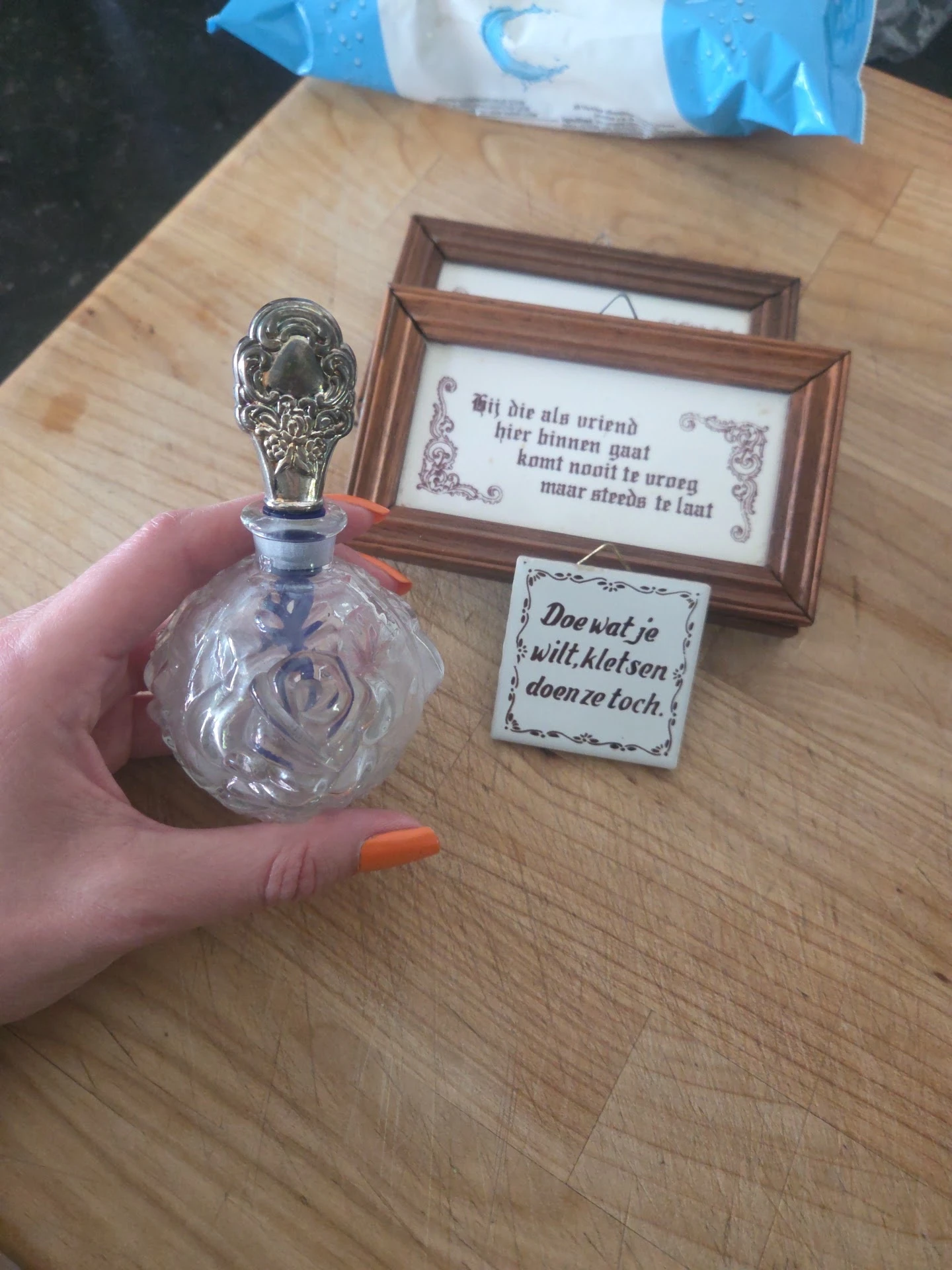 Close-up van een decoratieve glazen flesje met zilveren dop in de hand, met achtergrond van houten memobordjes met Nederlands