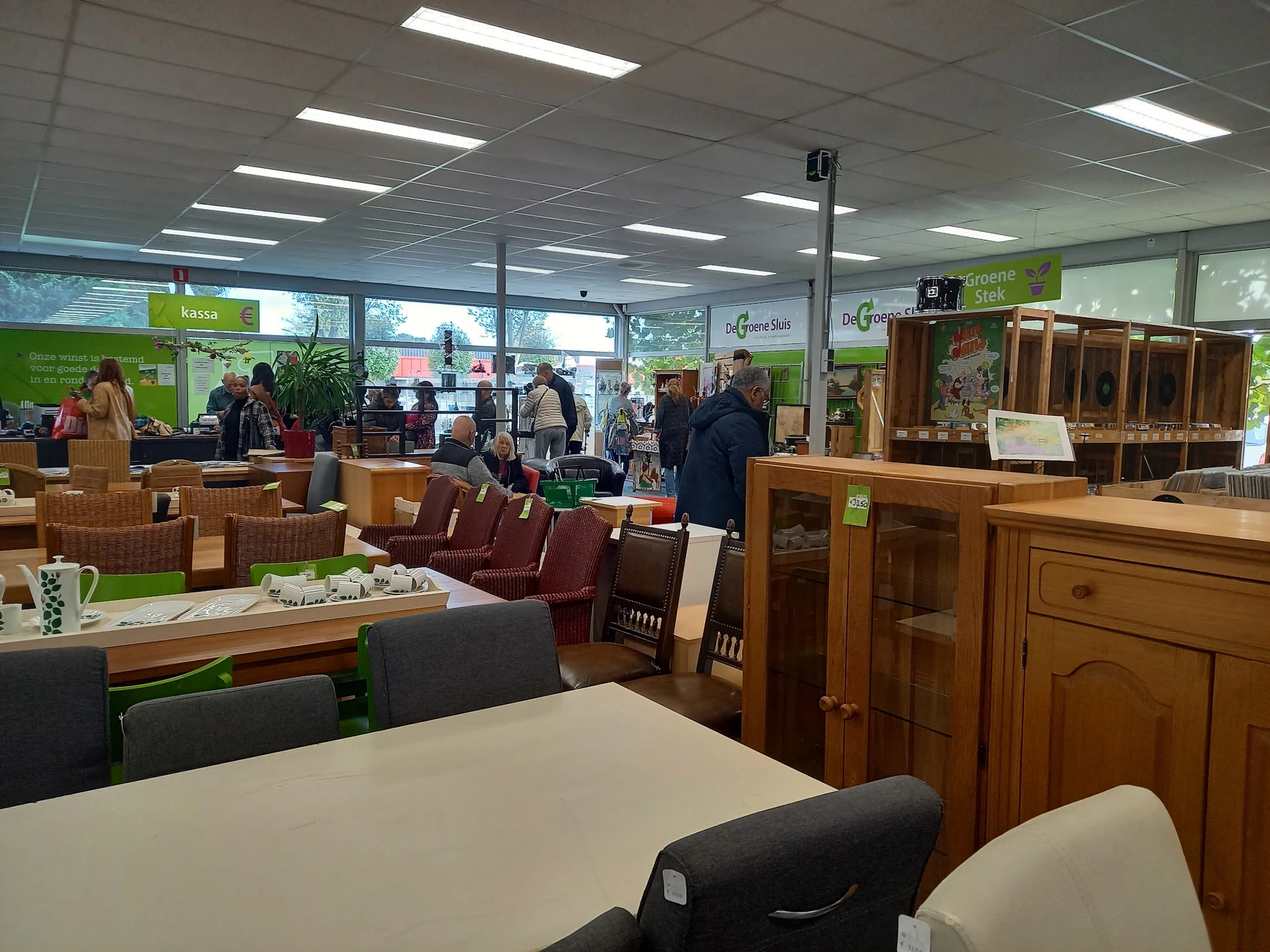 Winkelvloer met houten meubels, tafels en stoelen; klanten en personeel in het interieur van de kringloopwinkel