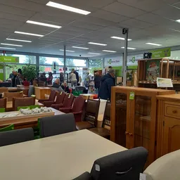 Winkelvloer met houten meubels, tafels en stoelen; klanten en personeel in het interieur van de kringloopwinkel
