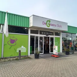 Groene gevel van kringloopwinkel met welkomstbord en glazen deuren aan de voorkant