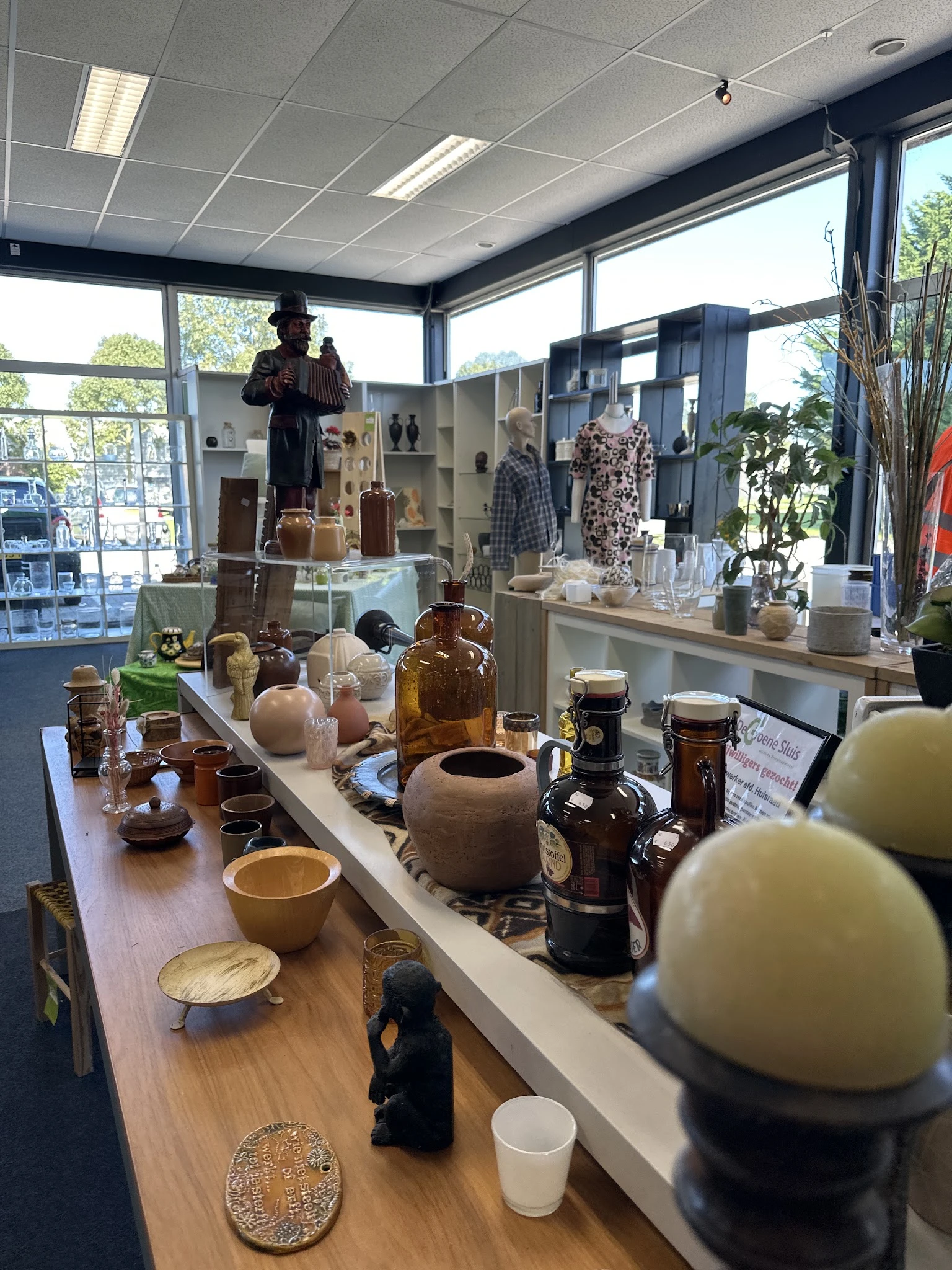 Uitgestalde tweedehands huishoudartikelen, vazen, glazen flessen en decoratieve items op een houten toonbank