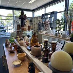 Uitgestalde tweedehands huishoudartikelen, vazen, glazen flessen en decoratieve items op een houten toonbank