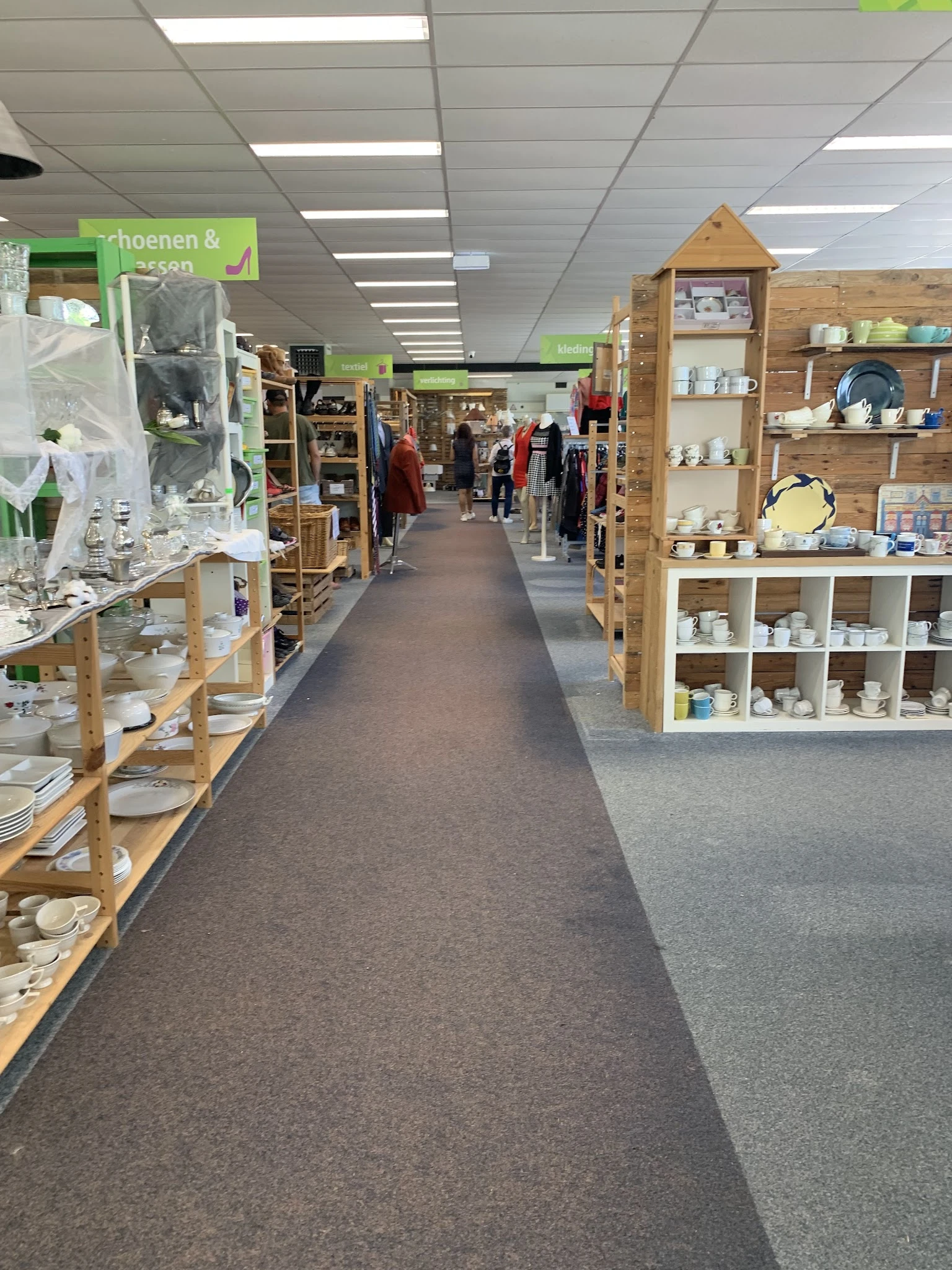 Winkelinterieur met houten stellingen, displaykasten met serviesgoed en kledingrekken langs de wanden