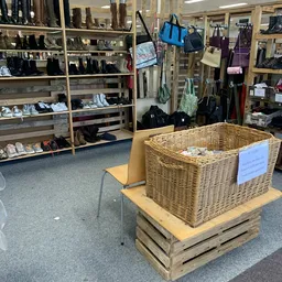Grote rieten mand vol met tweedehands items op houten platform in kringloopwinkel, met stellingen en kleding op de achtergron