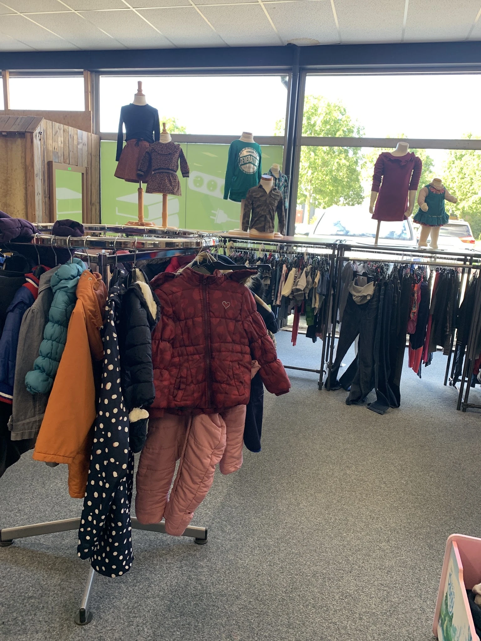 Rekken met tweedehands kinderkleding, waaronder jassen en broeken in verschillende kleuren