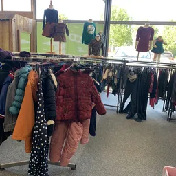 Rekken met tweedehands kinderkleding, waaronder jassen en broeken in verschillende kleuren