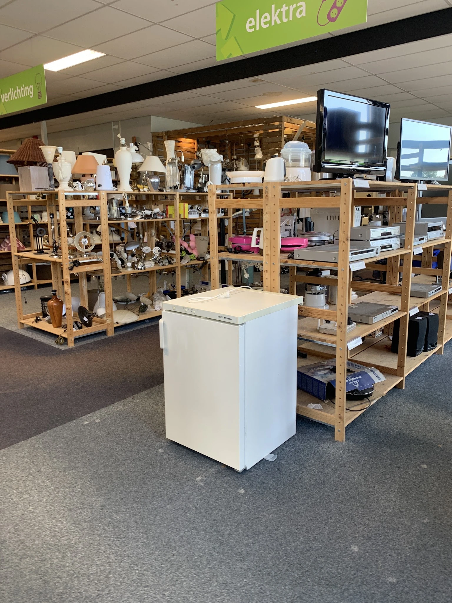 Winkelvloer met houten stellingen vol huishoudelijke spullen en een wit kastje in het midden