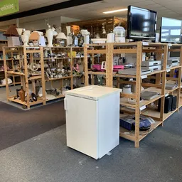 Winkelvloer met houten stellingen vol huishoudelijke spullen en een wit kastje in het midden