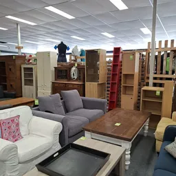 Winkelinterieur met diverse meubels: grijze bank, houten tafel, kasten en stellingen met opgestelde spullen