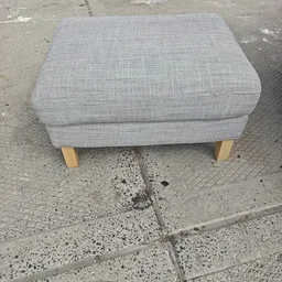 Grijze gestoffeerde poef of voetenbankje met houten poten op betonnen ondergrond