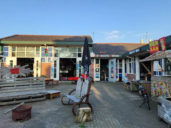 Voorgevel van kringloopwinkel met geel en blauw pand, ingang, etalage en terras met zitbanken