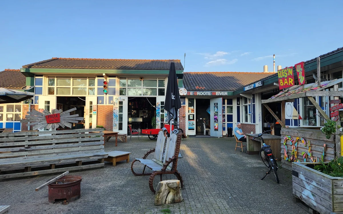 Voorgevel van kringloopwinkel met geel en blauw pand, ingang, etalage en terras met zitbanken