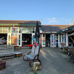 Voorgevel van kringloopwinkel met geel en blauw pand, ingang, etalage en terras met zitbanken