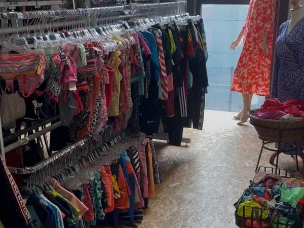 Winkelinterieur met kledingrekken vol tweedehands kleding, uitgestald op hangers en in manden