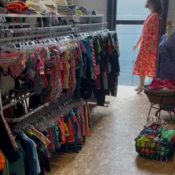 Winkelinterieur met kledingrekken vol tweedehands kleding, uitgestald op hangers en in manden