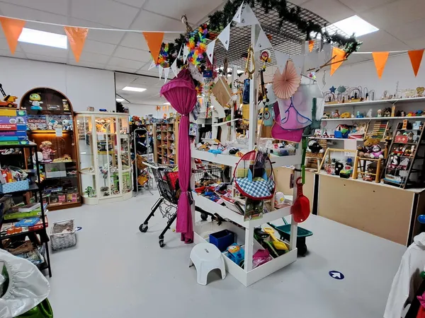 Winkelvloer met centrale display en opgehangen decoratie, omgeven door kasten en rekken met tweedehands goederen