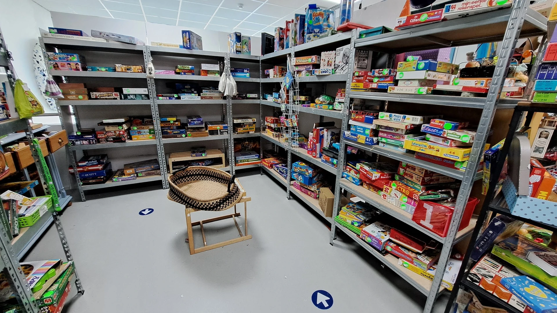 Winkelinterieur met metalen stellingen vol bordspellen, kaartspellen en speelgoed; houten stoel in het midden
