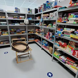 Winkelinterieur met metalen stellingen vol bordspellen, kaartspellen en speelgoed; houten stoel in het midden