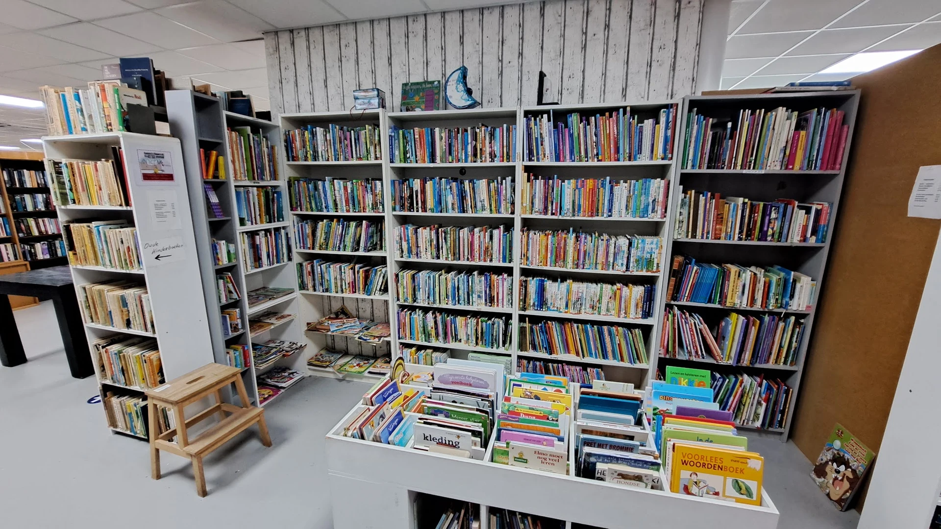 Boekenkasten met dvd's en boeken in een kringloopwinkel, met uitgestalde items op tafels vooraan