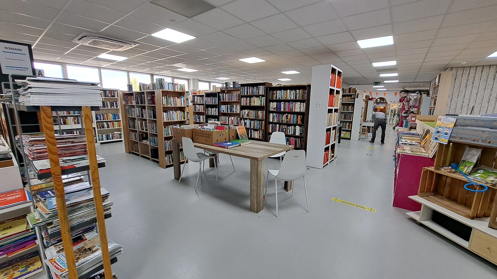 Winkelvloer met boeken in stellingen, leestafels en leeshoeken in een kringloopwinkel
