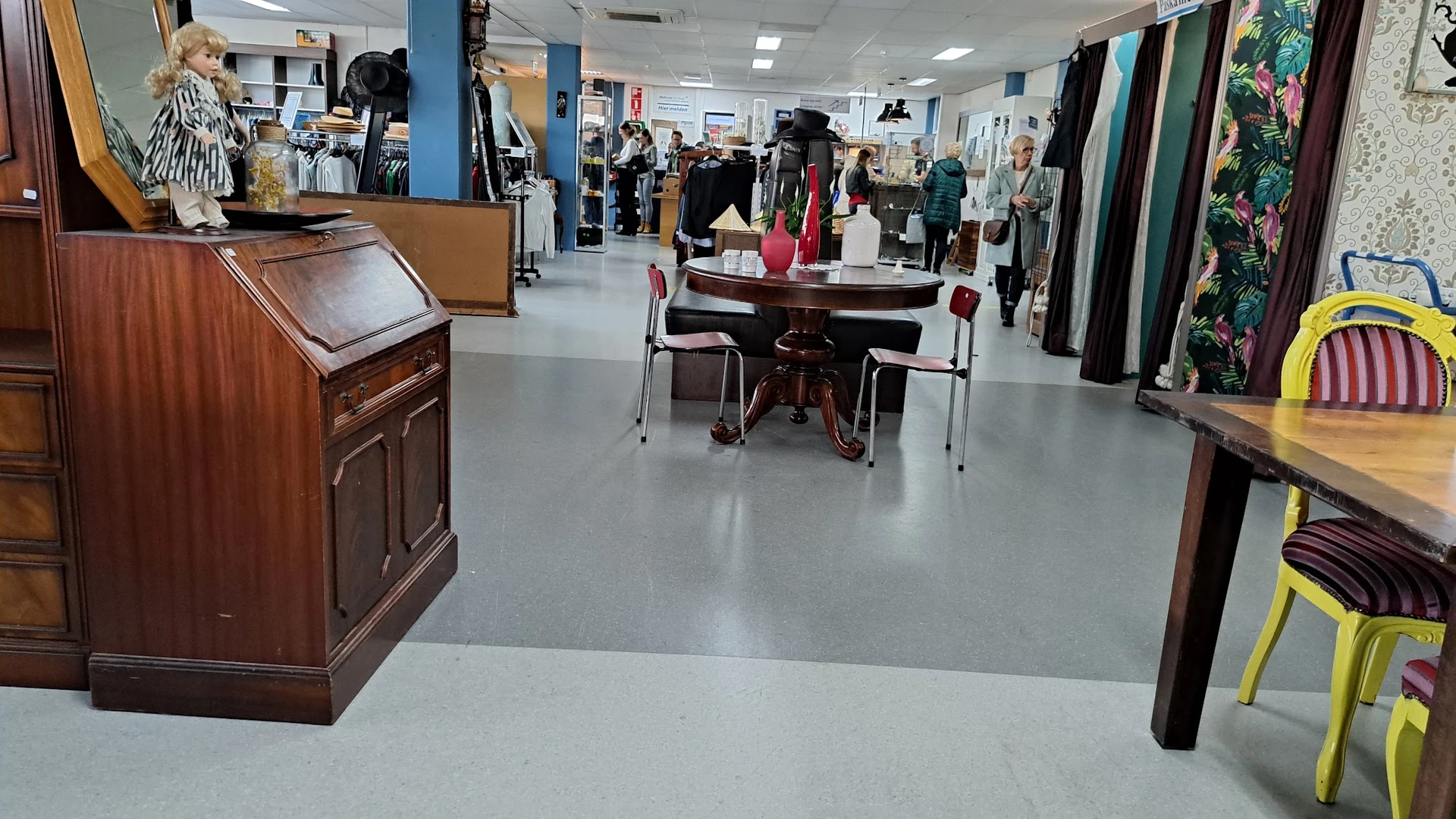 Winkelinterieur met kledingrekken, tafels met kledinguitstalling en bezoekers die winkelen