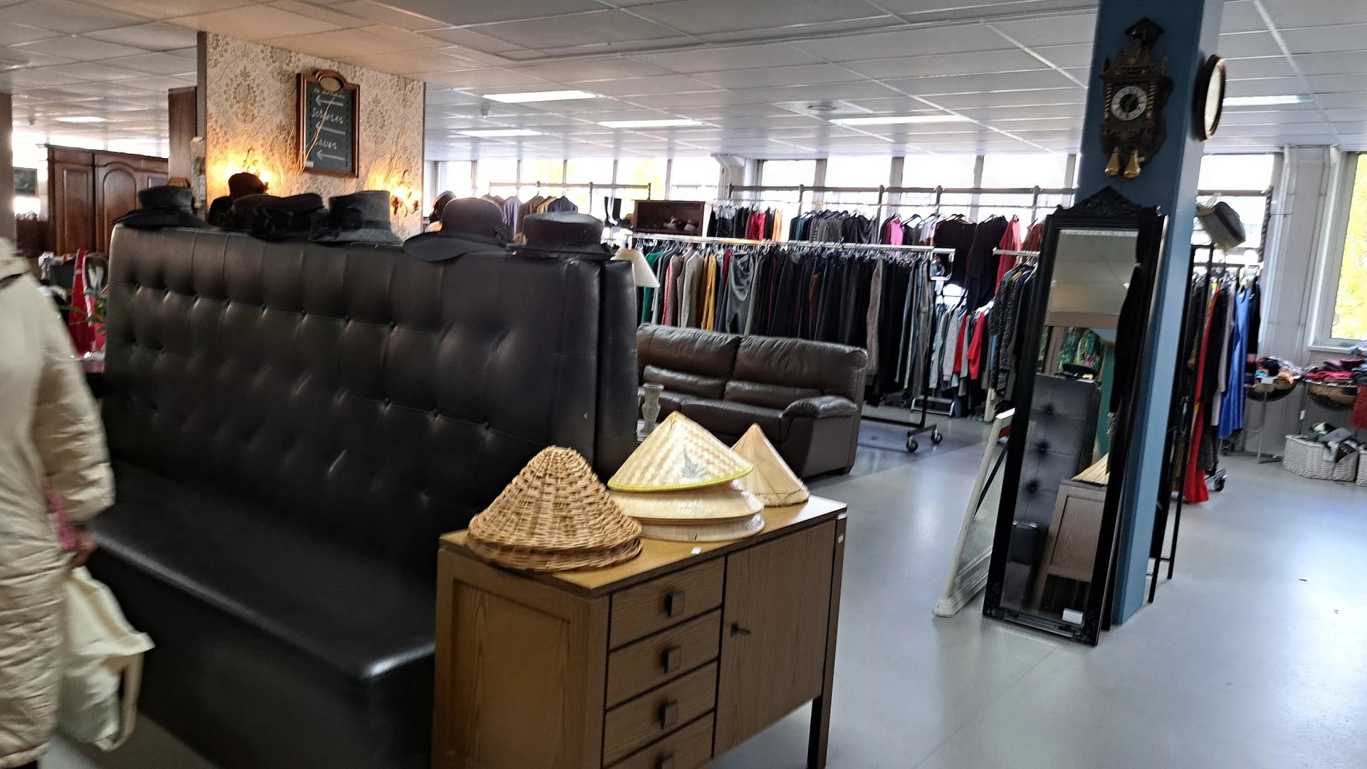 Winkelvloer met zitmeubelen, kledingrekken en accessoires zoals rieten hoeden op een houten kast