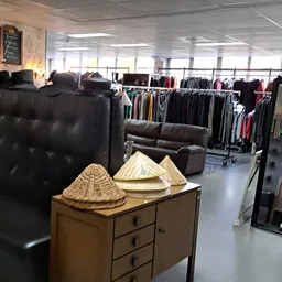 Winkelvloer met zitmeubelen, kledingrekken en accessoires zoals rieten hoeden op een houten kast
