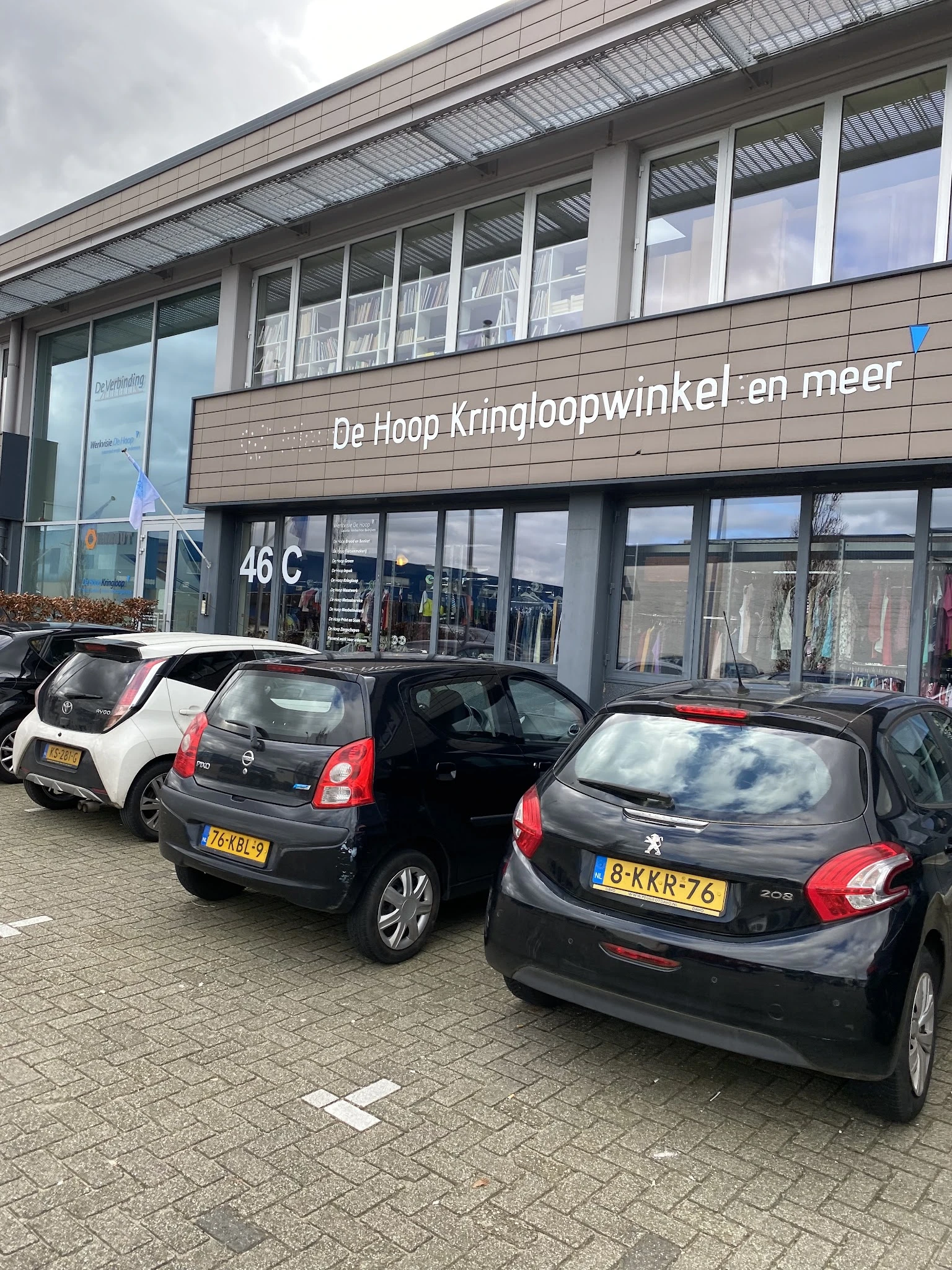 Voorgevel van kringloopwinkel met parkeerplaatsen en geparkeerde auto's ervoor