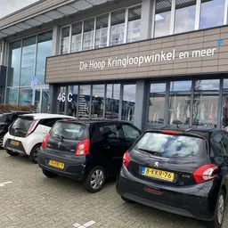 Voorgevel van kringloopwinkel met parkeerplaatsen en geparkeerde auto's ervoor