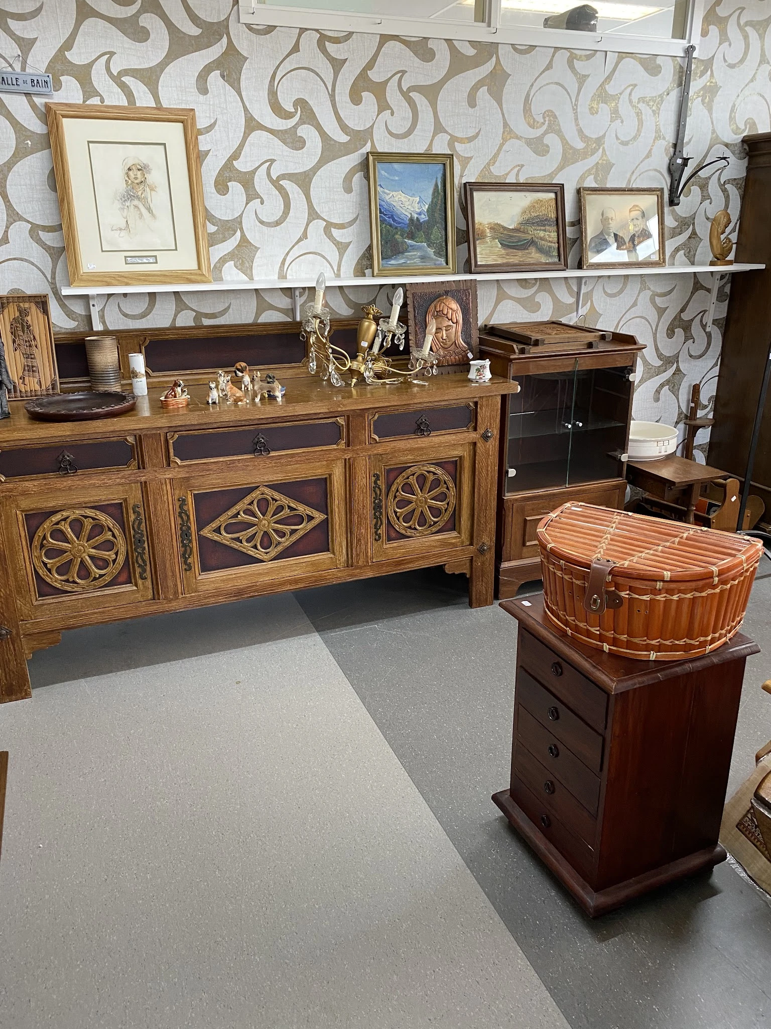 Houten dressoir met ingelegd houtwerk en decoratieve panelen, met daarnaast een houten koffer en ander antiek meubilair