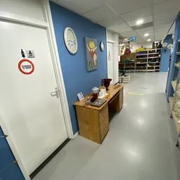 Winkelruimte met blauwe wanden, houten toonbank, klokken aan de muur en stellingen met spullen op de achtergrond