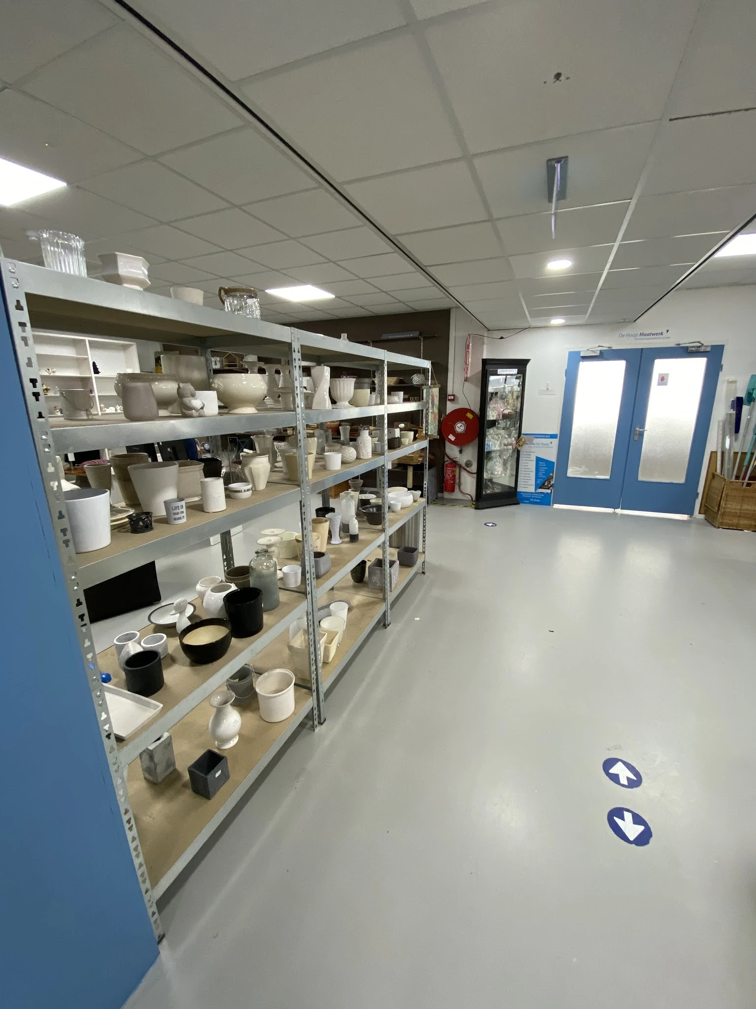 Metalen stellingen met wit serviesgoed, kopjes, schalen en keramische items in een kringloopwinkel