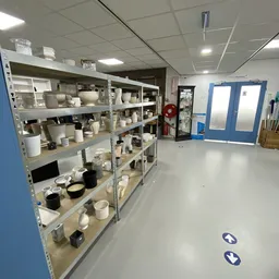Metalen stellingen met wit serviesgoed, kopjes, schalen en keramische items in een kringloopwinkel