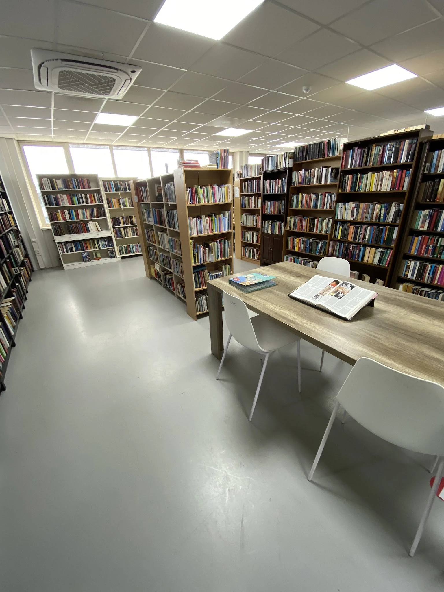 Bibliotheekruimte met boekenkasten langs de wanden en een houten tafel met witte stoelen in het midden