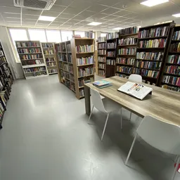 Bibliotheekruimte met boekenkasten langs de wanden en een houten tafel met witte stoelen in het midden