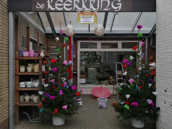 Winkelentree met naam 'de KEERKRING' boven deur, versierd met kleurrijke bloemen in potten