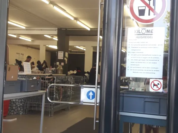 Binnenaanzicht van kringloopwinkel met stellingen, tafels en enkele klanten aan het winkelen