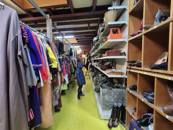 Winkelvloer met kledingrekken links en houten stellingen met schoenen en accessoires rechts