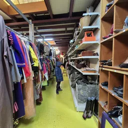 Winkelvloer met kledingrekken links en houten stellingen met schoenen en accessoires rechts