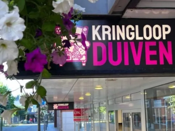 Zwart winkelgevelbord met 'KRINGLOOP DUIVEN' in wit en roze letters, omgeven door bloemen