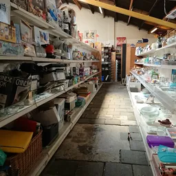 Lange gang in een kringloopwinkel met volle stellingen vol spullen aan beide zijden