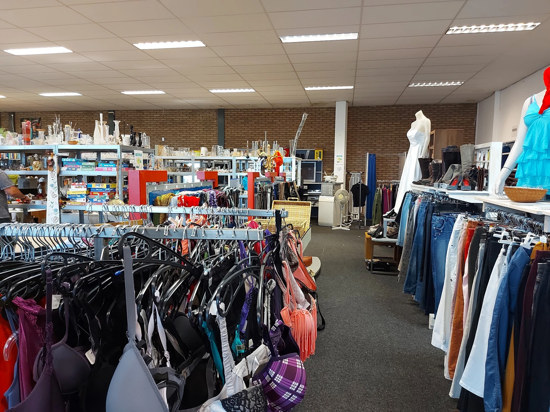 Winkelvloer van kringloopwinkel met rekken vol kleding aan hangers, toonpoppen en stellingen met spullen