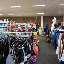 Winkelvloer van kringloopwinkel met rekken vol kleding aan hangers, toonpoppen en stellingen met spullen