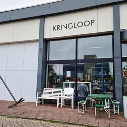 Gevel van kringloopwinkel met witte en grijze panelen, grote ramen, zitgroep buiten op terras