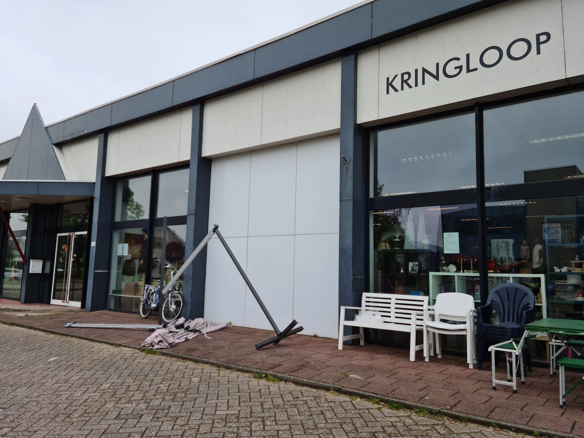 Moderne gevel van kringloopwinkel met witte panelen en zwarte ramen, winkelname KRINGLOOP zichtbaar, ingang links met fiets e