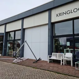 Moderne gevel van kringloopwinkel met witte panelen en zwarte ramen, winkelname KRINGLOOP zichtbaar, ingang links met fiets e
