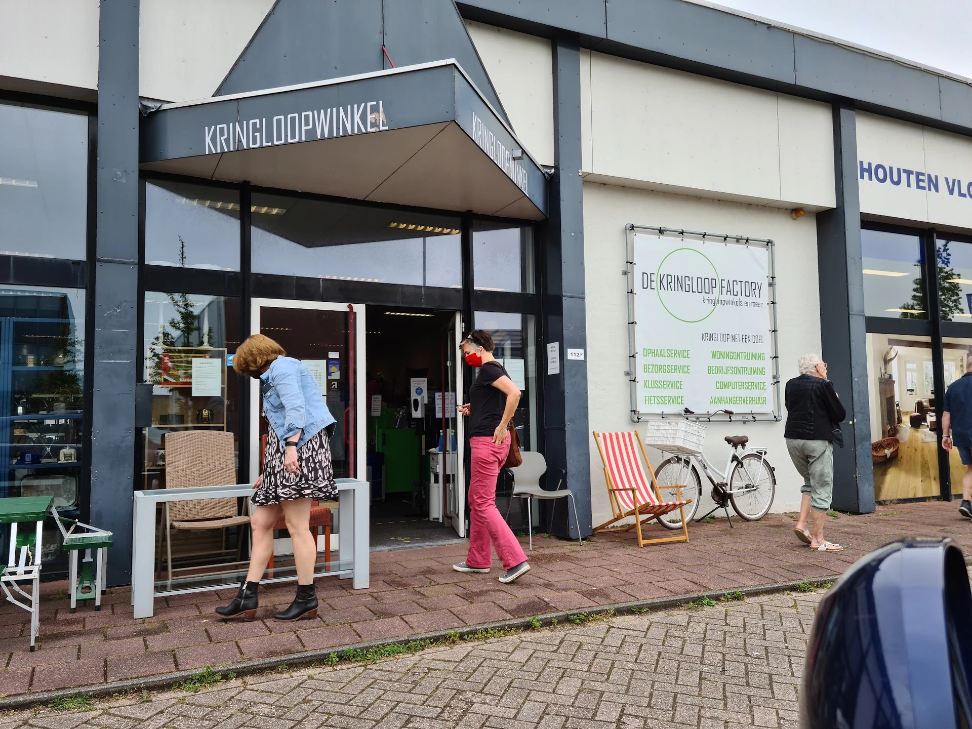 Winkelgevel van Kringloopwinkel met donker frame, witte pui en entree, zithoeken en fiets op het terras